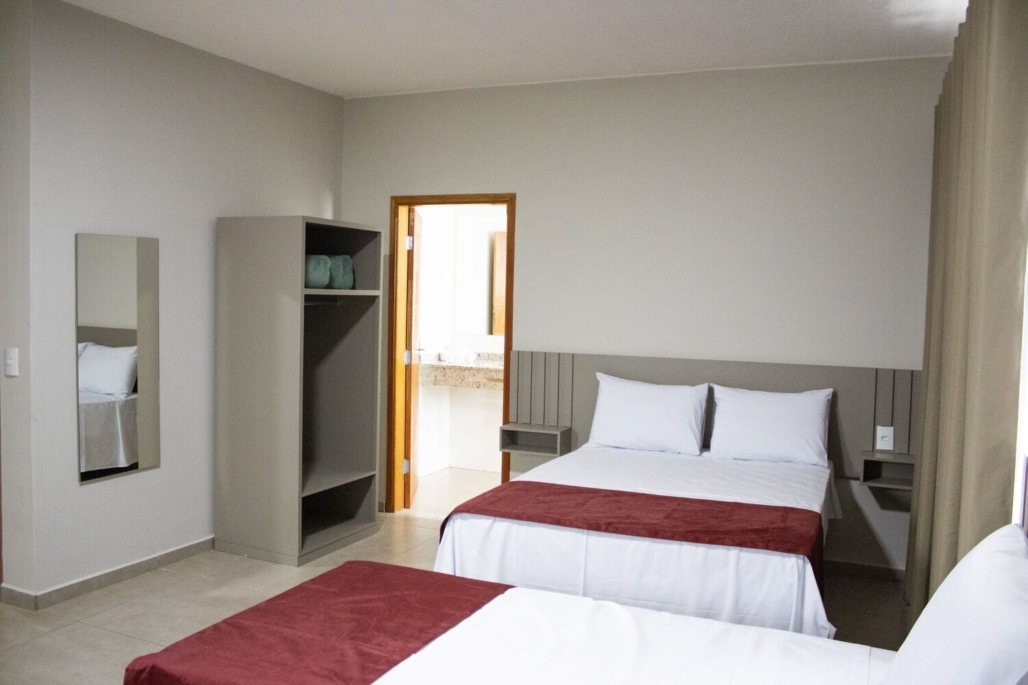 Una habitación de hotel con dos camas, un armario, un espejo y una puerta que da a un balcón.