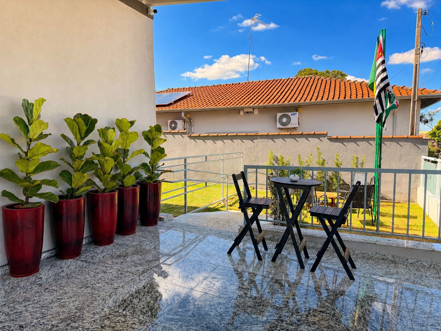 A terrace with potted plants, a table with chairs, and a flag.