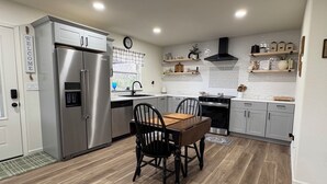 Een moderne keuken met een roestvrijstalen koelkast, een eettafel met stoelen, een fornuis en een klok aan de muur.