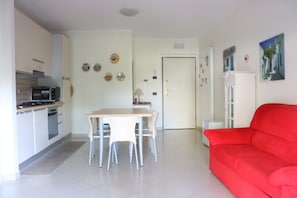A modern kitchen with a dining area, a red sofa, and a door leading to another room. - Homiday - Raffaella, Three Bedroom Apartment with Balcony (Alba Adriatica)
