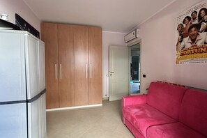 Ein Zimmer mit einem weißen Kleiderschrank, einem rosa Sofa und einem Poster an der Wand.
