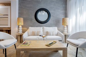 Un salon moderne avec un canapé, deux tables d’appoint, une table basse et un miroir rond accroché au mur.