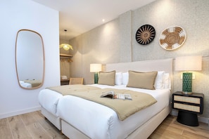 Une chambre d’hôtel moderne avec un grand lit, deux tables de chevet avec des lampes, une horloge murale et un miroir.