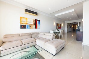 A modern living room with a sectional sofa, a glass coffee table, and abstract wall art. - The Strand - 3BED SliemaSeafront Fl 3 by Homely (Tas-Sliema)