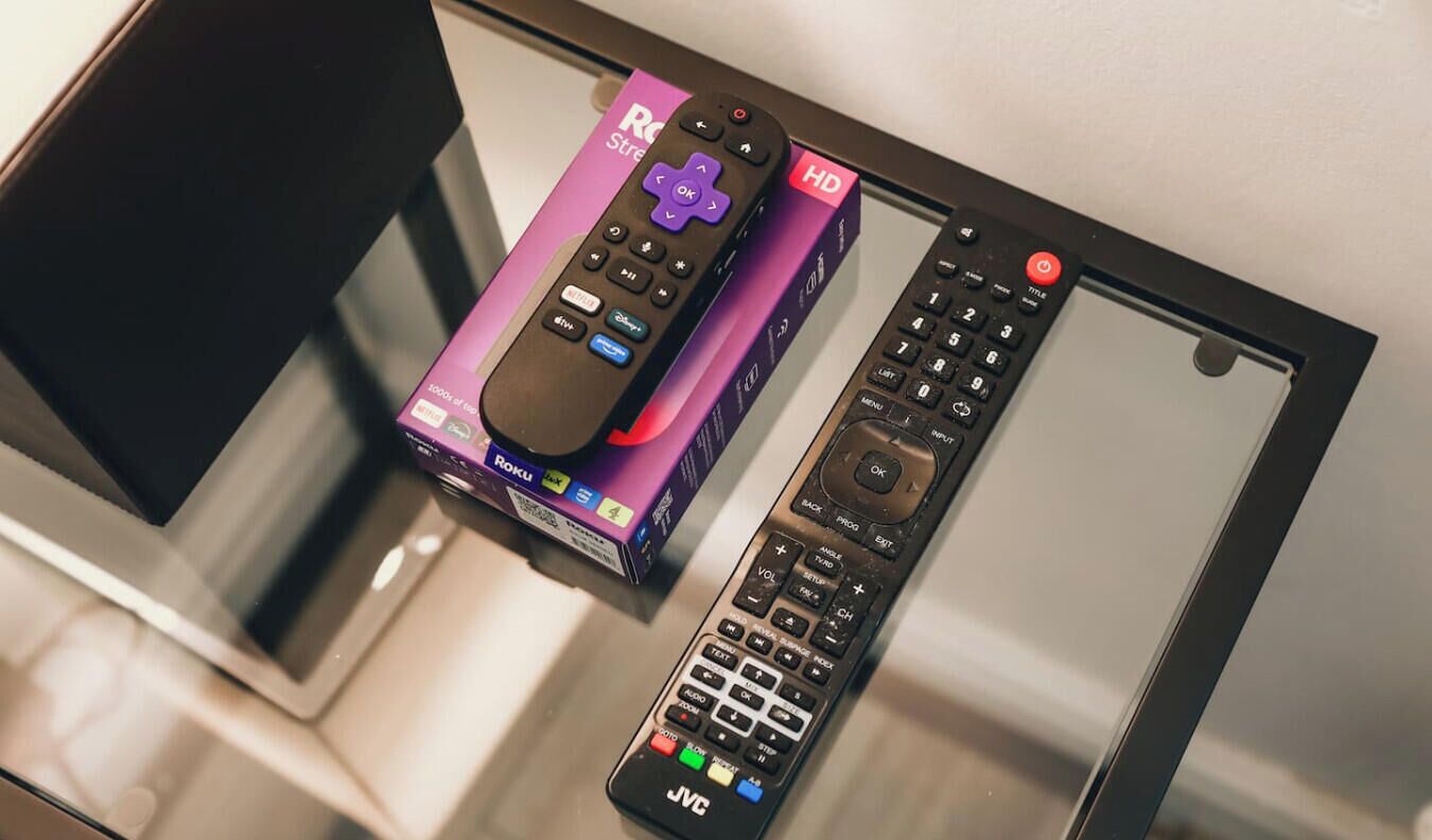 A glass table with a Roku box and two remote controls.