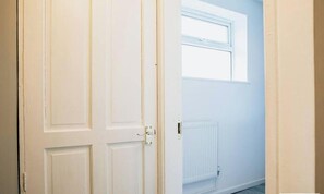 A white door with a window above it, a radiator below, and a light switch on the wall. - Flora`s Flat 3 - Studio Apartment in Sneinton (Nottingham)