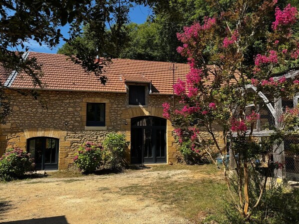 Un edificio de piedra con techo de tejas, puerta principal y una ventana pequeña.