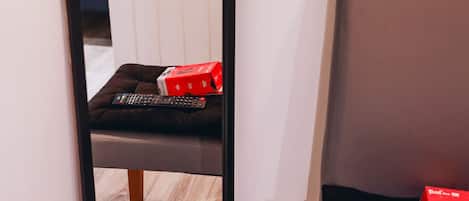 A room with a wooden floor, a black chair, a red box, and a remote control.