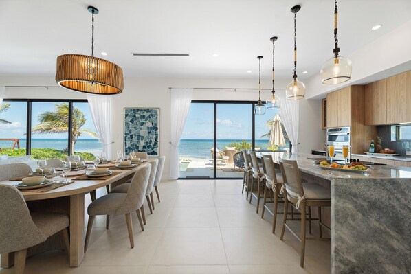 A modern kitchen with a large island, dining area with chairs, and a view of the ocean.