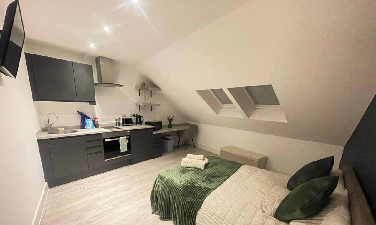 Ein gemütliches Schlafzimmer mit Bett, Nachttisch, Schreibtisch und einer kleinen Küchenzeile.