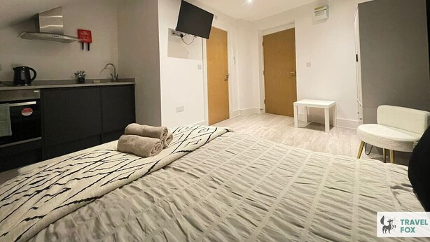 Ein Hotelzimmer mit Bett, Fernseher, einer Küchenzeile, einem Sessel und einem kleinen Tisch.