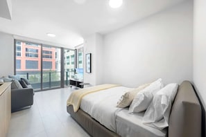 Ein modernes Hotelzimmer mit einem großen Bett, einer Sitzecke, einem Schreibtisch und einem Balkon mit Blick auf die Stadt.