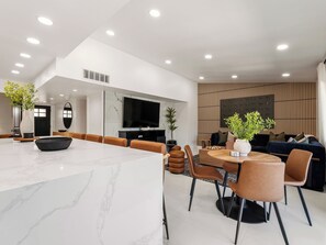 A modern living room with a large TV, seating area, and a dining table. - Poolside Playhouse / Ultimate Game Room + Pool (The Colony)