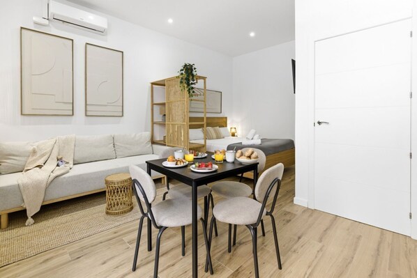 Une chambre d’hôtel moderne avec un canapé, une table à manger avec des chaises, un lit et une porte blanche.