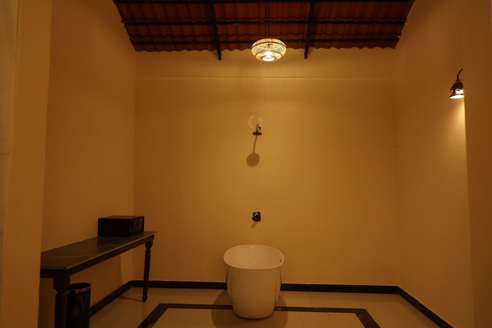 Un baño con inodoro, un cesto de basura, una mesita pequeña e iluminación empotrada en la pared.