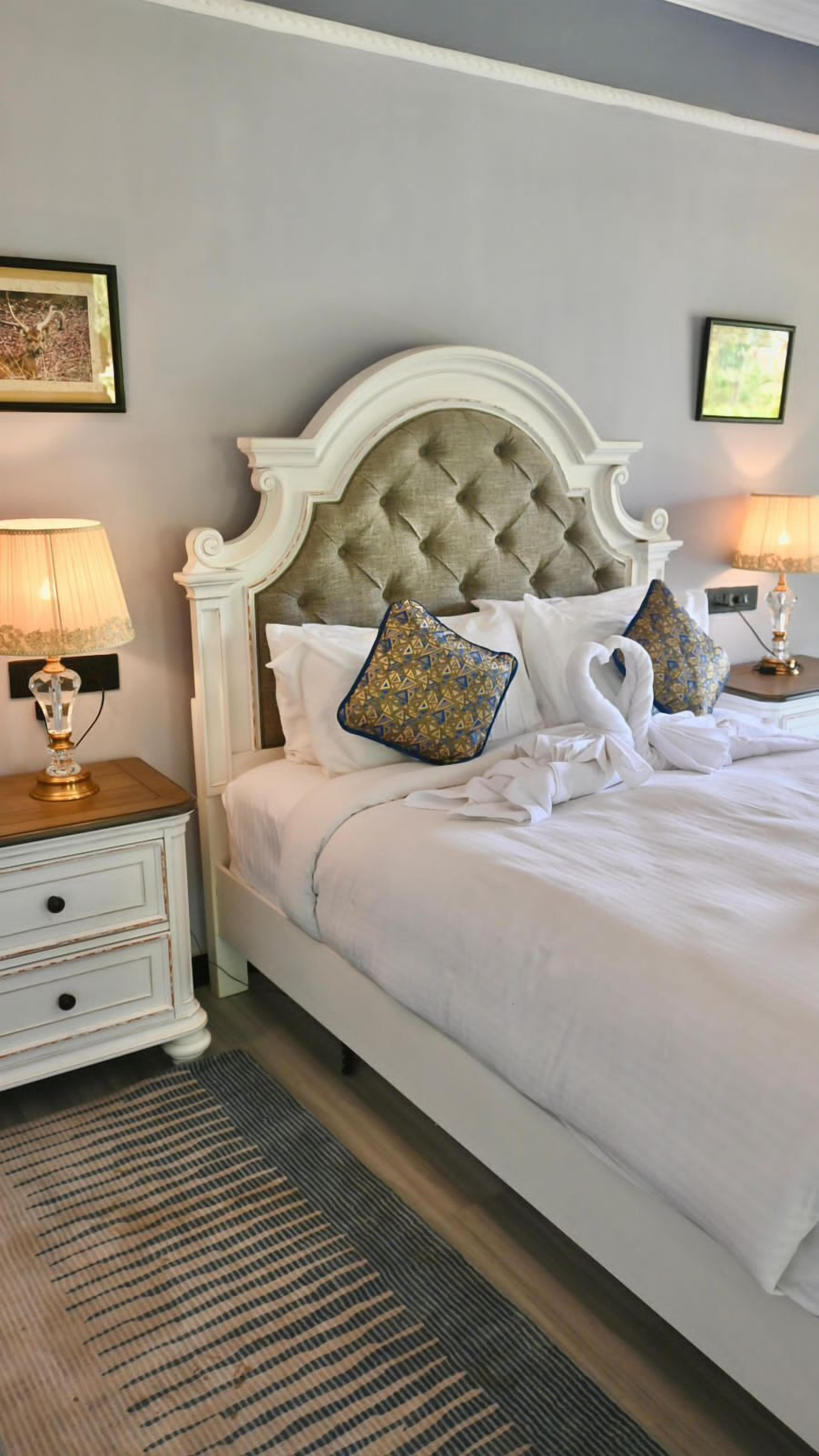Una cama bien hecha con un cabecero capitonado, dos almohadas decorativas, una lámpara de noche y un pequeño mueble con cajones.
