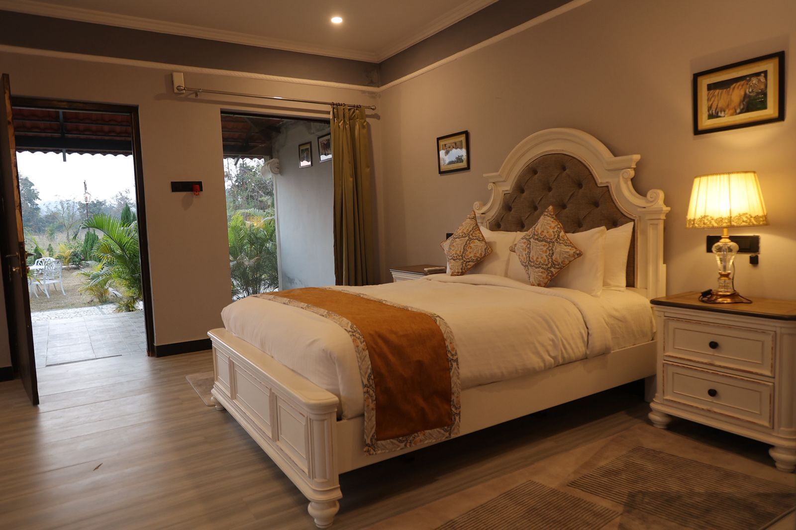 A bedroom with a large bed, a nightstand with a lamp, a door leading to a balcony, and a framed picture on the wall.