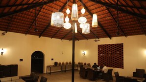 Un espace de restauration intérieur doté de hauts plafonds, de luminaires suspendus et d’un mur décoré de motifs. Des tables et des chaises sont disposées pour accueillir les convives.