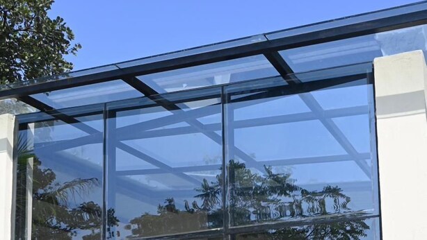 Un bâtiment moderne doté de grandes fenêtres en verre, d’un mur extérieur blanc et d’un espace extérieur aménagé avec des chaises.