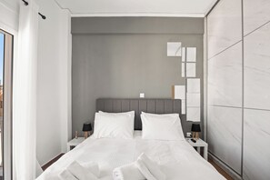 A modern hotel room with a large bed, two bedside tables with lamps, a grey headboard, and a view of the city through the window. - Luxury 2BR Penthouse Marina & Sea Views (Pireas)