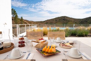 A table set with breakfast items, a view of a pool, and a mountainous landscape.