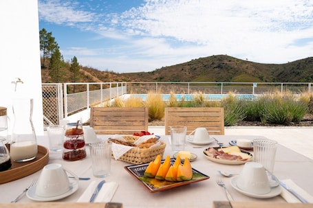 A table set with breakfast items, a view of a pool, and a mountainous landscape.. Studio 'Este' – Monte de Torquines