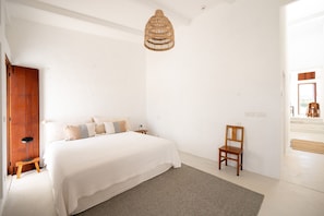 Une chambre à coucher comprenant un lit, une chaise, un lampadaire et un luminaire en matière tressée.
