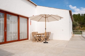 Une terrasse avec une table et des chaises, un parasol et une porte-fenêtre coulissante.