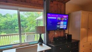 Een kamer met een televisie waarop een Roku-interface wordt weergegeven, een houten terras zicht, een witte stoel en een zwarte dressoir.