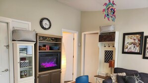 Een woonkamer met een open haard, een blauwe fauteuil, een donkere bank en een boekenkast.
