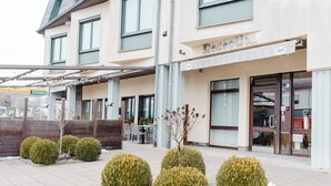 A hotel with a covered outdoor seating area, a reception desk, and a visible entrance. - Hotel Casa56 (Weiswampach)