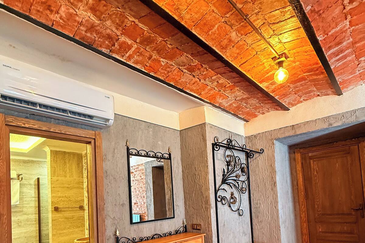 Una habitación con suelo de madera en patrón espiga, un banco de madera, un espejo y una lámpara fijada a la pared.