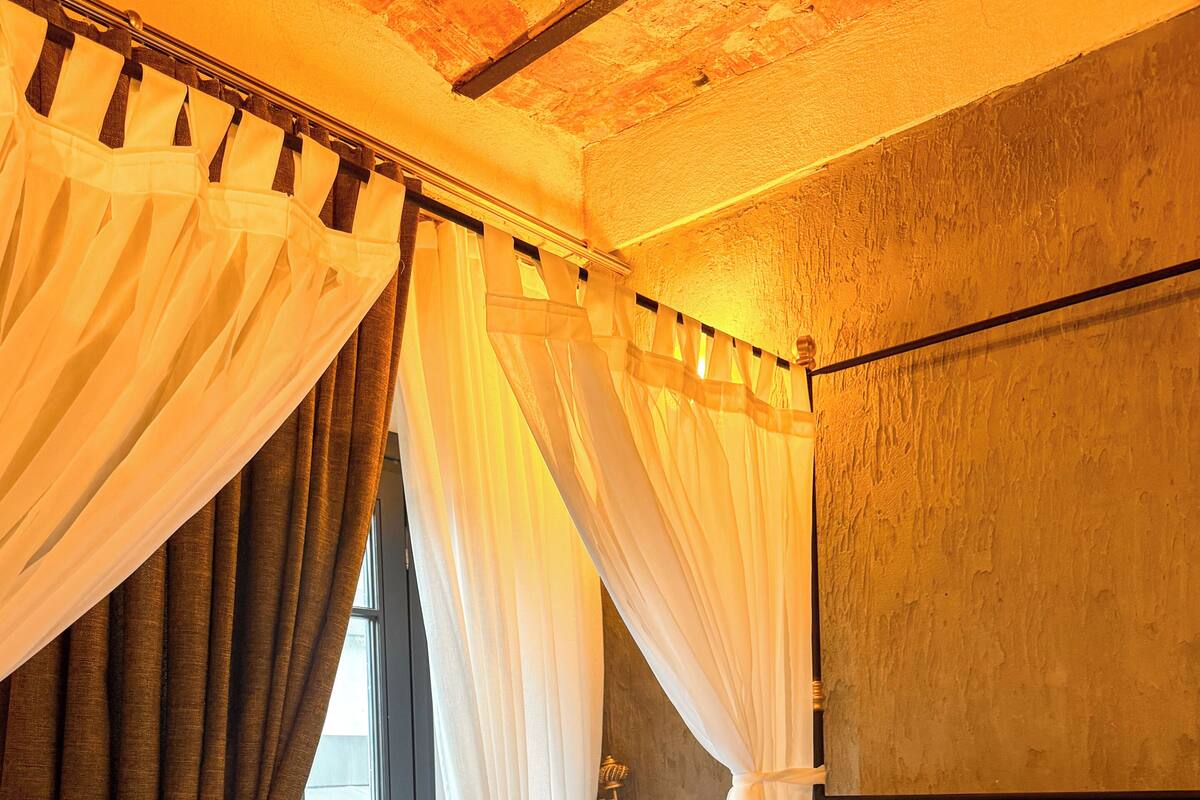 Un dormitorio con cama, cortinas, una mesita de noche y una ventana.