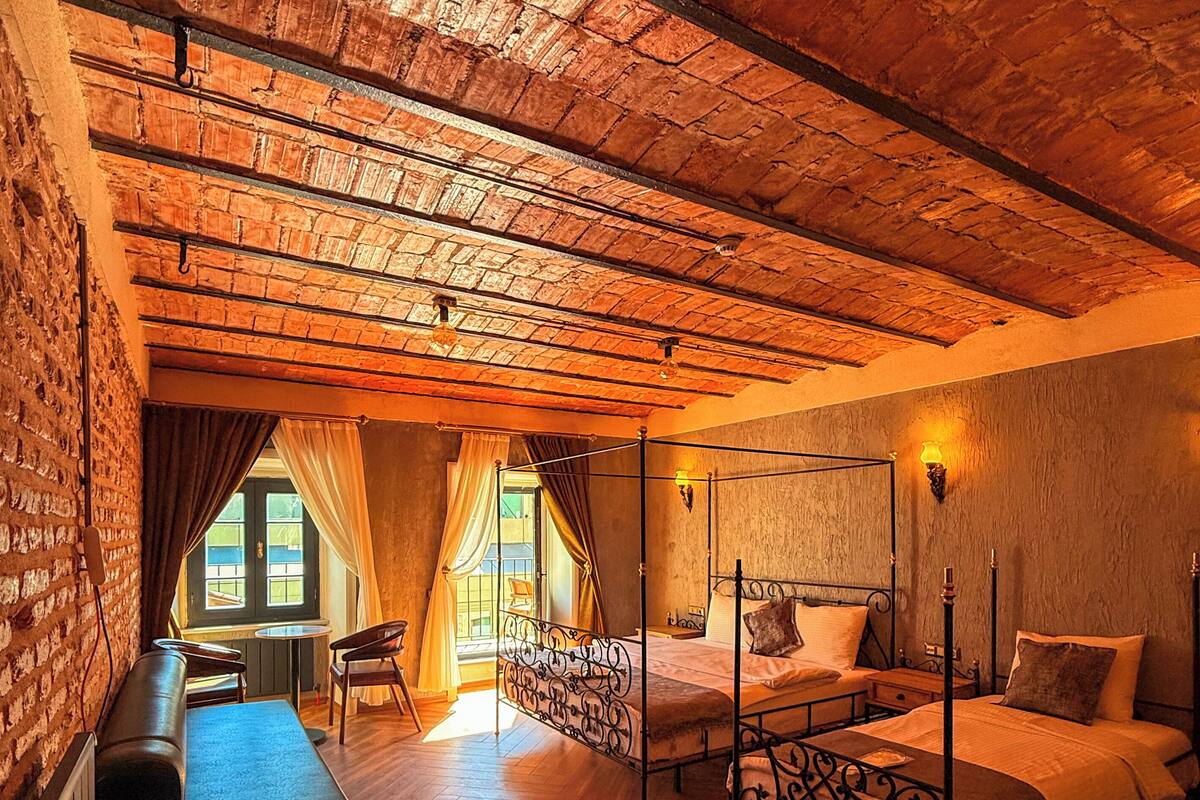 Una habitación con cama con dosel, un sofá, una mesita y vistas al exterior a través de una ventana.