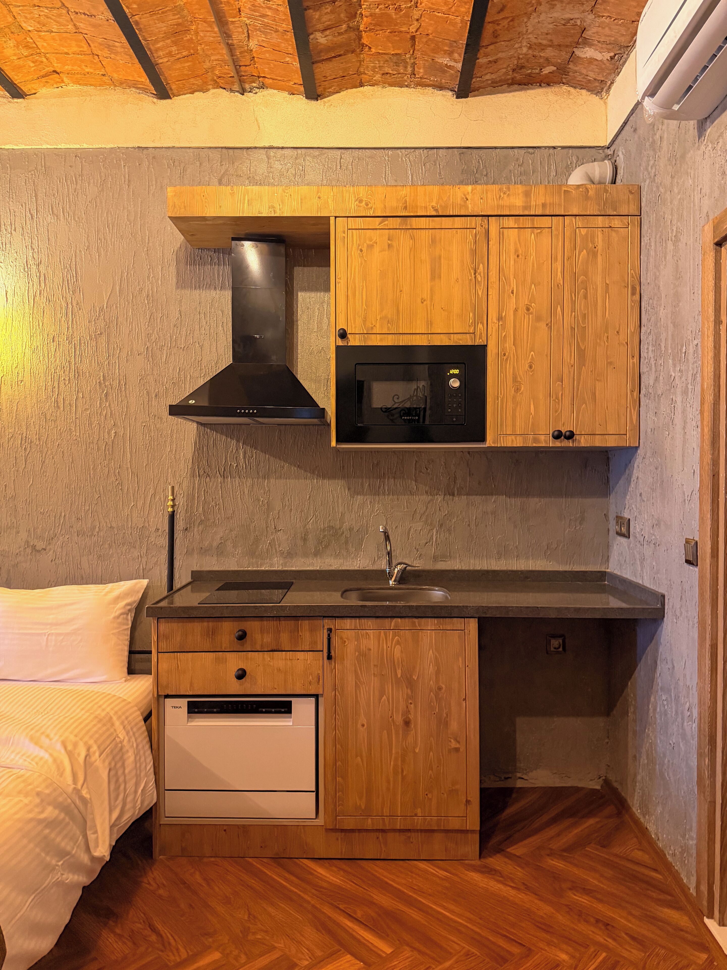 Una cocina compacta con armarios de madera, un microondas, una estufa y un lavabo.
