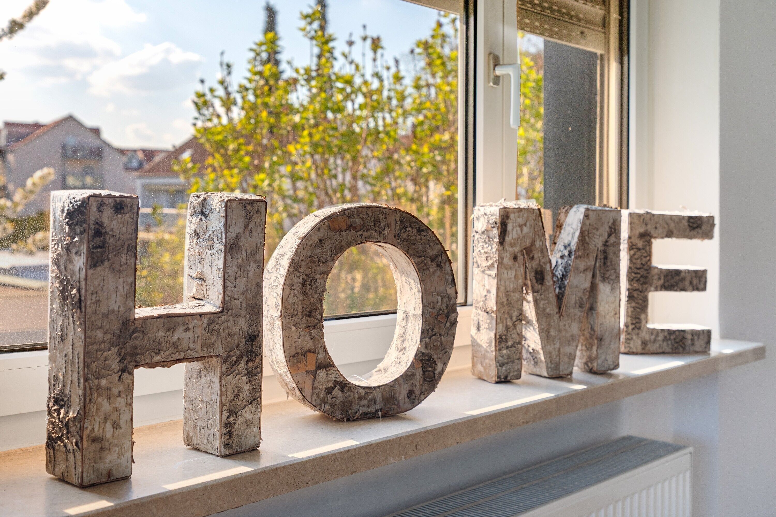 Holzbuchstaben mit dem Wort 'HOME' auf einer Fensterbank.