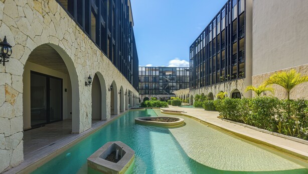 A swimming pool with stone walls and arched openings, surrounded by greenery and modern buildings. - 3 Mi to Beach! Tranquil Tulum Oasis w/ Balcony (Tulum)