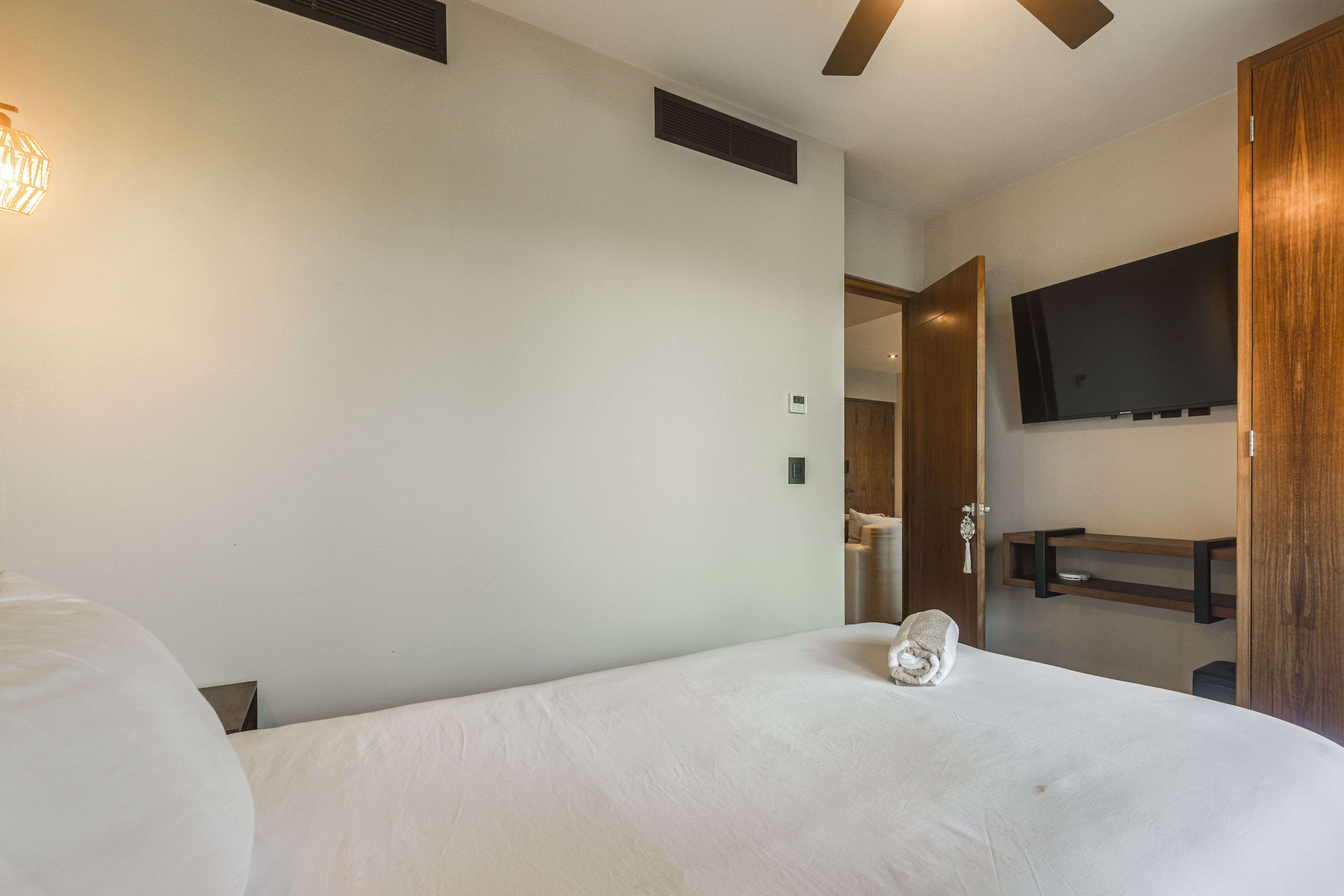 Une chambre d’hôtel avec un lit, un ventilateur de plafond, un téléviseur fixé au mur et une porte en bois.