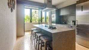 A modern kitchen with a central island, bar stools, stainless steel appliances, and a view of greenery outside. - 3 Mi to Beach! Tranquil Tulum Oasis w/ Balcony (Tulum)
