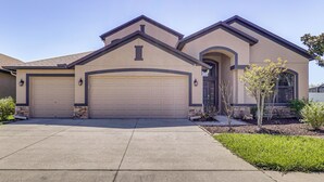A two-story house with a garage, a front entrance, and a small garden. - Extended Stay in Tampa Area! Spacious Home w/ Yard (Riverview)