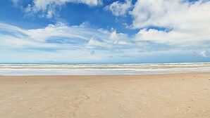 A wide sandy beach with gentle waves and a clear blue sky with scattered clouds. - Sweeping View, Luxe Perks: Suntide III - Unit 708 (South Padre Island)