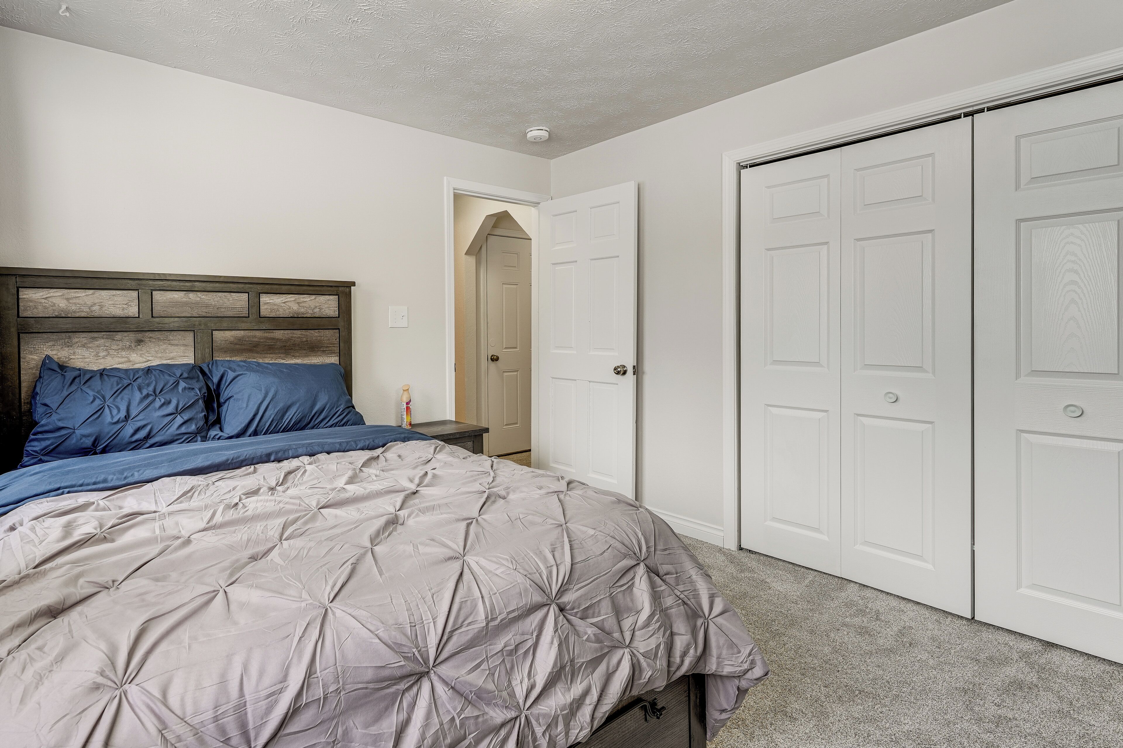 Une chambre à coucher comprenant un lit, une table de chevet, une armoire et une porte donnant sur une autre pièce.