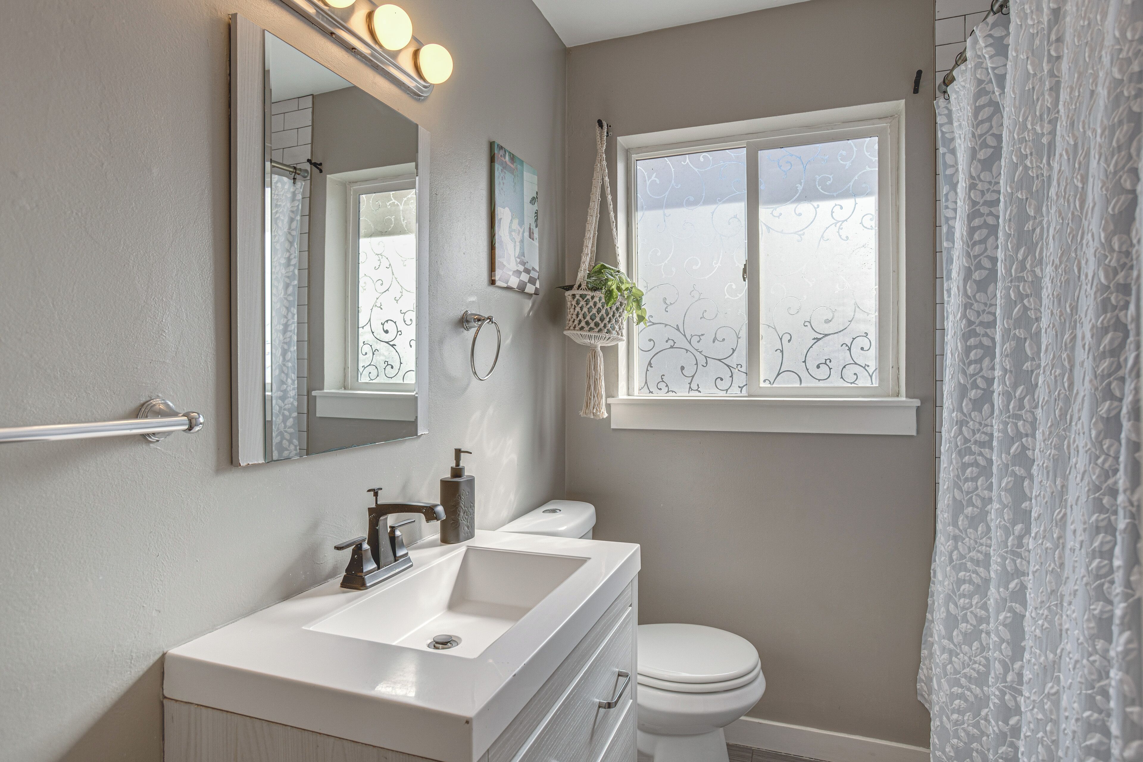 A bathroom with a sink, mirror, toilet, and window with a view.