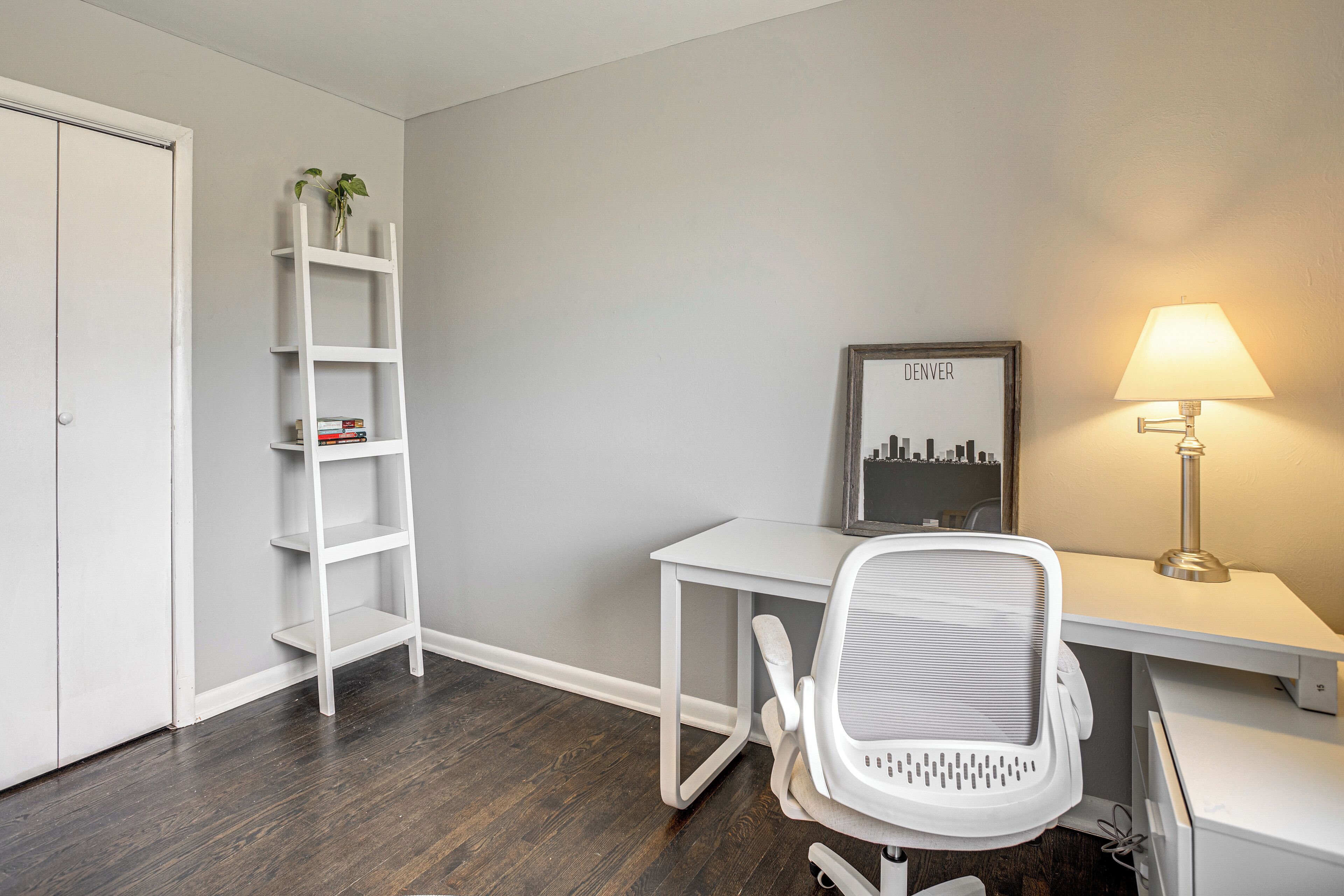 A room with a white desk, a white chair, a white shelving unit, a framed picture, and a lamp.