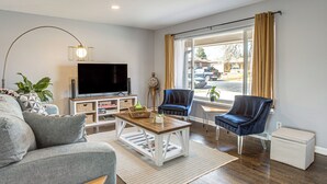 A living room with a sofa, a coffee table, a TV, a chair, and a window with curtains. - Family Friendly! Spacious Lakewood Haven w/ Yard (Lakewood)
