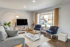 A living room with a sofa, a coffee table, a TV, a chair, and a window with curtains. - Family Friendly! Spacious Lakewood Haven w/ Yard (Lakewood)