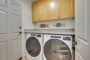 A laundry room with two front-loading washers, wooden cabinets above, and a fish-shaped decoration on the wall. - Beach Club & Pool at Big Island Resort Getaway! (Kamuela)