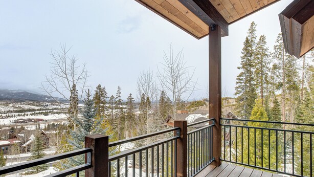 Eine Holzterrasse mit Metallgeländer, mit Blick auf eine verschneite Landschaft mit Bäumen und Gebäuden.