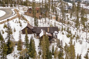 A wooden cabin with a curved driveway, surrounded by snow-covered trees.