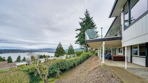 Una casa moderna con una zona esterna coperta, vista su un lago e su una collina.